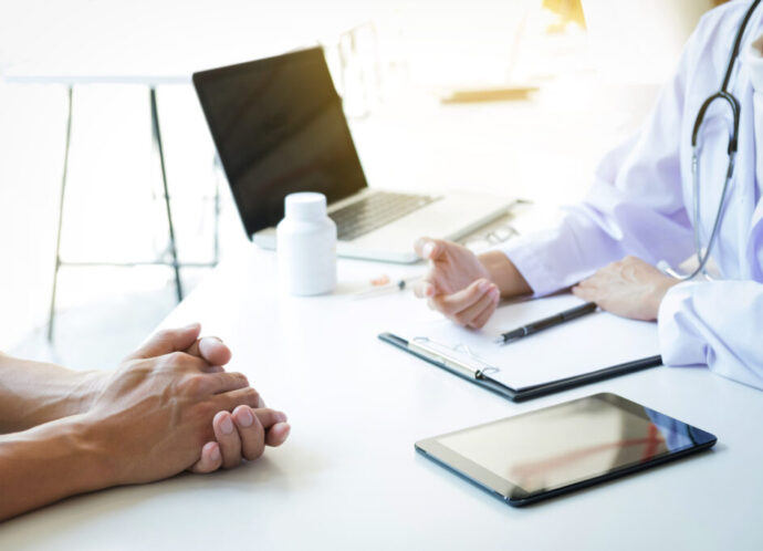 Close-Up Of Doctor And Patient Discussing At Table In Office
